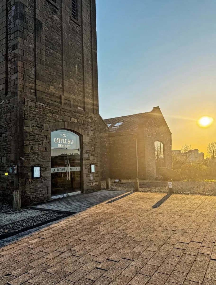 A stone building with a Cattle & Co Smokehouse sign on the glass doors, at sunset