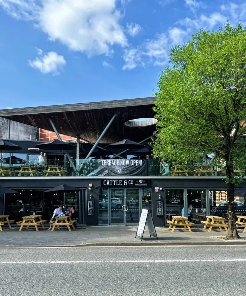 The Cattle & Co frontage with picnic benches on the terrace and trees in leaf