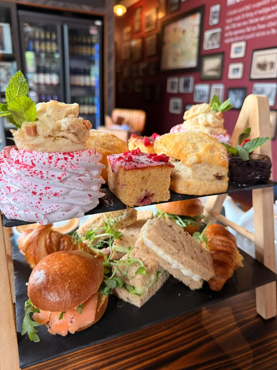 An afternoon tea stand with cakes and scones above finger sandwiches and a slider