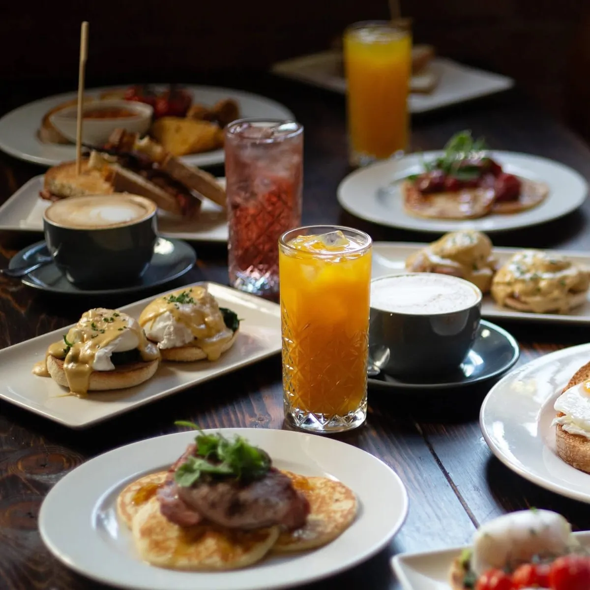 A brunch table with eggs Benedict, pancakes, coffees and fresh juice